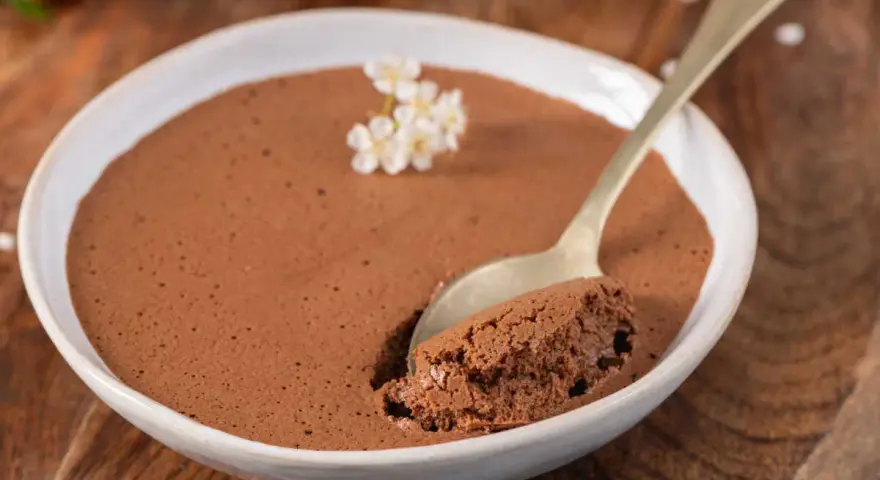 Une cuillère prend une bouchée d'une mousse au chocolat facile et aérienne, garnie de petites fleurs blanches.