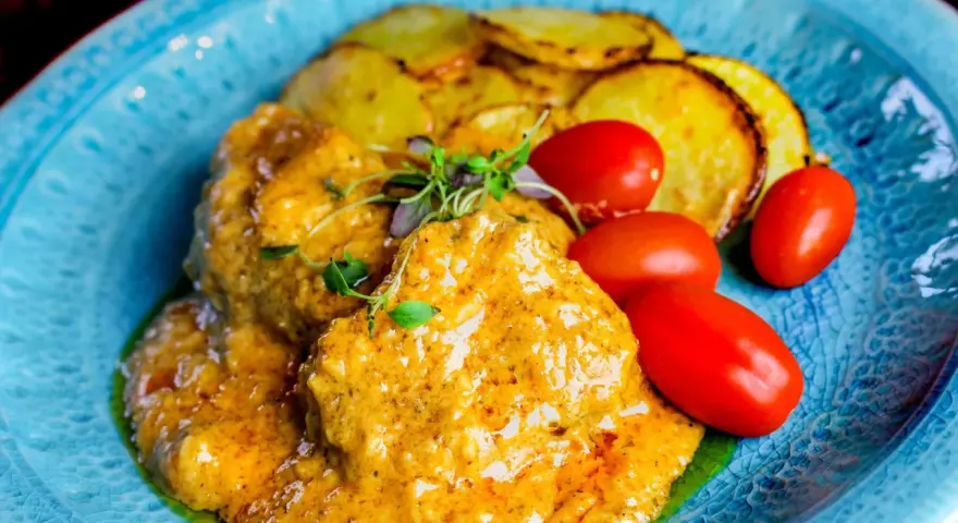 Köttbullar i krämig cafe de paris sås med rostade potatisskivor och körsbärstomater på en blå tallrik.