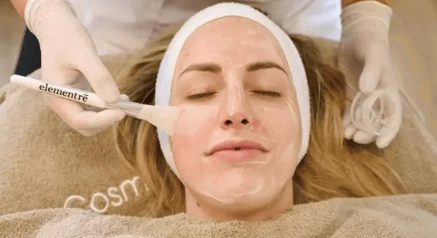 Kosmetikerin trägt eine Maske auf, um die Haut zu reinigen.