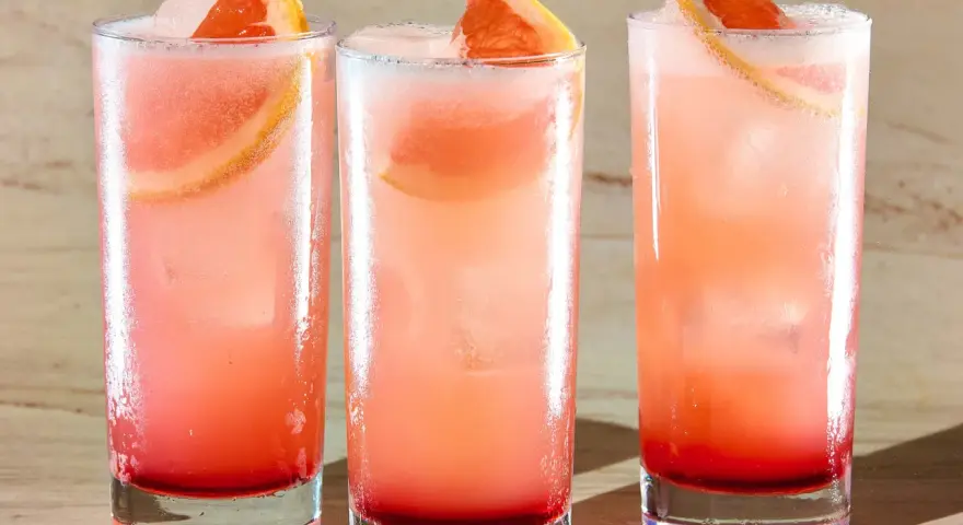 Trzy orzeźwiające drinki: Tequila Sunrise i Paloma, z plasterkami grejpfruta i lodem.