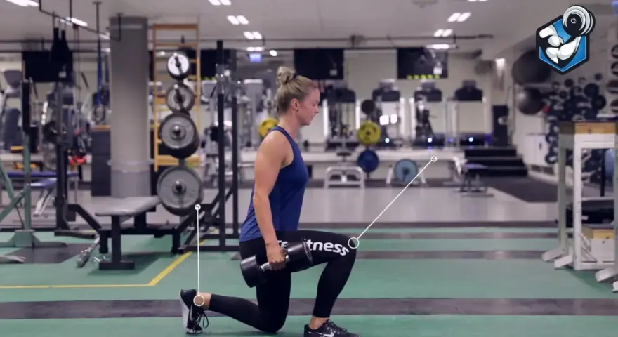 Kvinna utför utfallssteg med vikt i ett gym. Hon håller en hantel i ena handen och har ett ben framåt och ett bakåt.