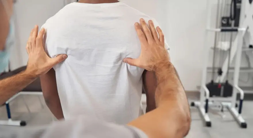 Fizjoterapeuta bada plecy pacjenta, oceniając kręgosłup piersiowy pod kątem objawów neurologicznych.