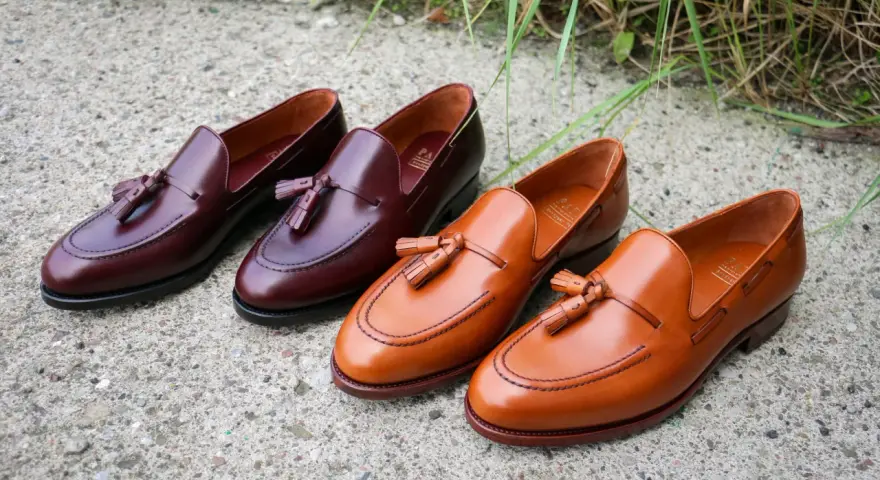 Eleganckie, skórzane loufersy z chwostami w kolorze koniaku i burgundu, ułożone na betonowej nawierzchni.