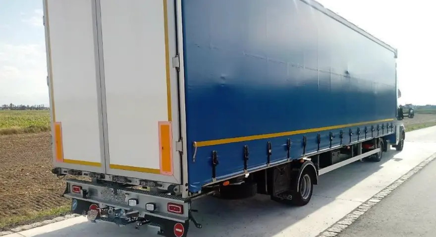 Ciągnik siodłowy z niebieską plandeką i białymi drzwiami naczepy, widok z tyłu i boku.