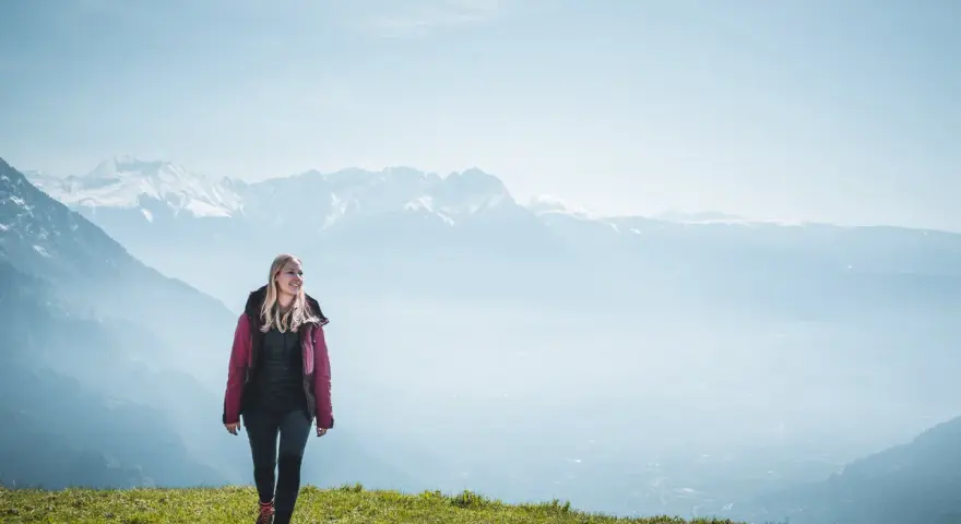 Frau in Wanderkleidung genießt die Aussicht auf verschneite Berge. Perfekt, was zieht man zum wandern an!