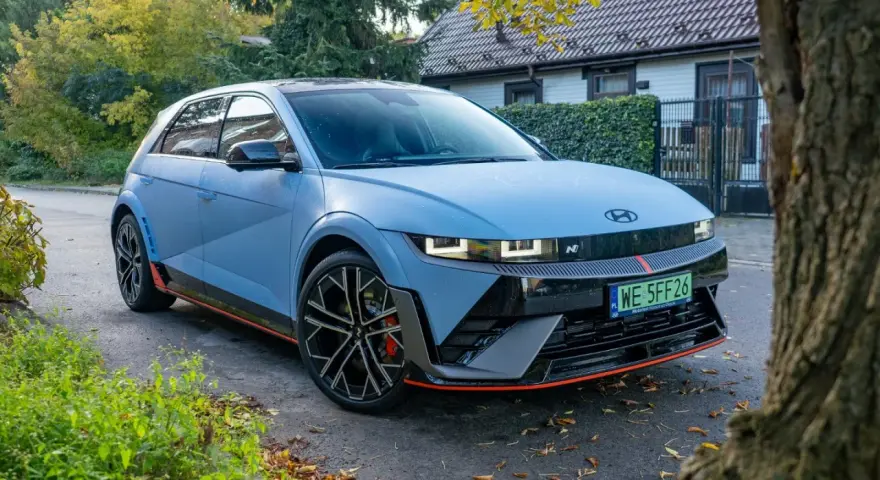 Niebieski Hyundai Ioniq 5 N z czerwonymi akcentami stoi na tle domu i drzew.