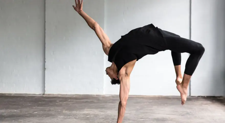 Un bailarín en un estudio blanco realiza un movimiento acrobático, mostrando que es la danza.