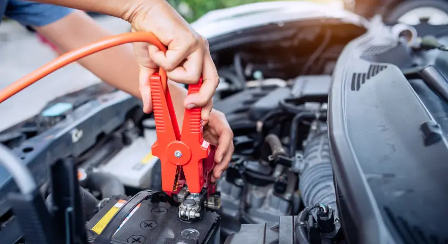Hands connect jumper cables to a car battery, a common fix when wondering how long can a car be on before the battery dies.