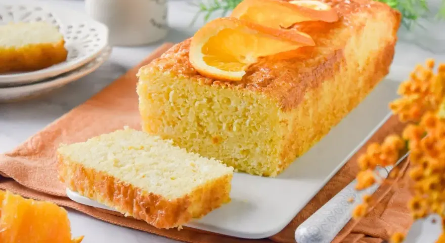 Un delicioso bizcocho de naranja, recién horneado y decorado con rodajas de naranja. Perfecto para acompañar un café.