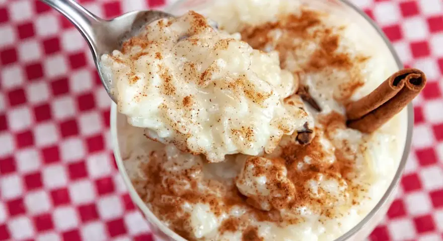 Cuchara con cremoso arroz con leche, espolvoreado con canela. ¿Quién inventó el arroz con leche? ¡Este postre es un clásico!