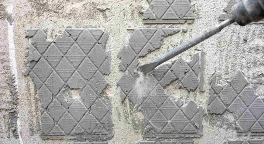 Outil de burinage en action pour enlever colle carrelage sur un mur en béton.