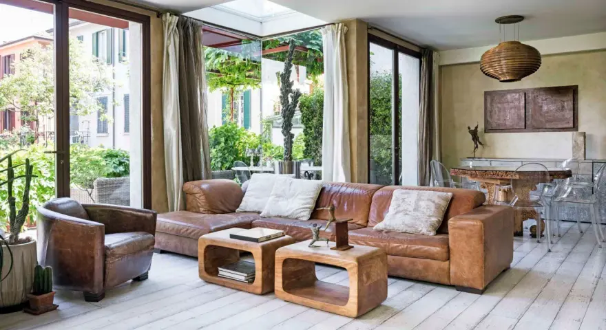 Accogliente soggiorno etnico chic con divano in pelle, poltrona vintage e vista sul verde.