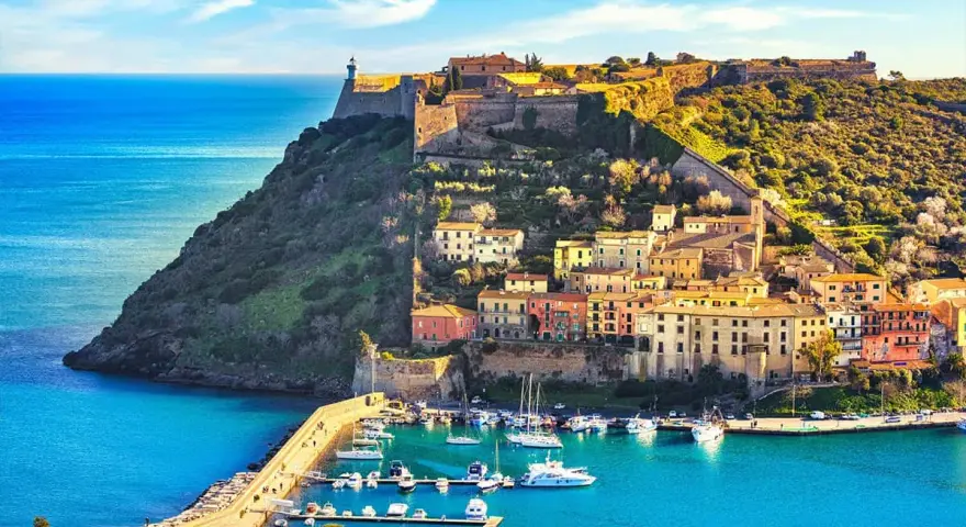 Incantevoli toscana paesaggi: un borgo colorato su una collina fortificata domina un porto con barche, baciato dal sole.