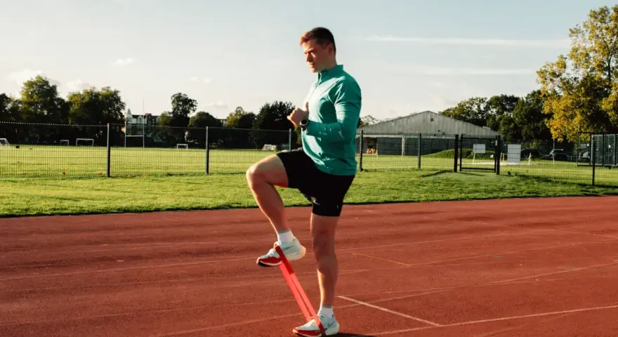 Uomo si allena con elastico sulle caviglie in pista, pronto a riprendere a correre.