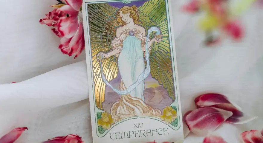 La carta de la templanza tarot, con su figura etérea vertiendo agua, rodeada de pétalos de tulipán rosa y blanco, evoca serenidad y equilibrio.
