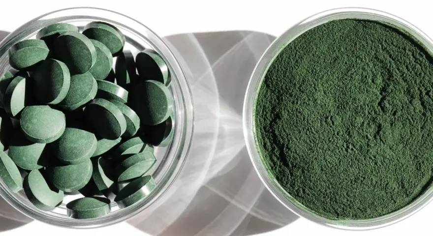 Dwie szklane miseczki: jedna z tabletkami chlorelli, druga z zielonym proszkiem. Dowiedz się, chlorella jak stosować, by czerpać z niej korzyści.
