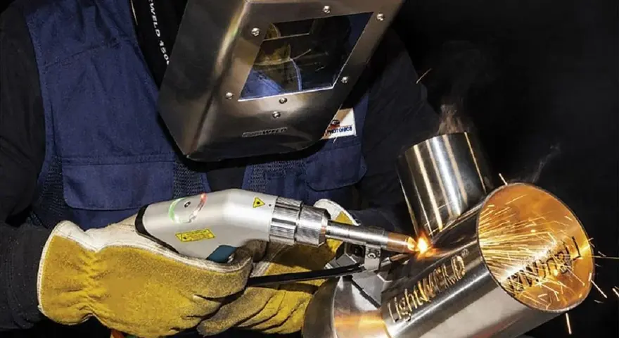 Operator w masce spawalniczej wykonuje napawanie laserowe metalowych elementów, tworząc iskrzące spoiny.