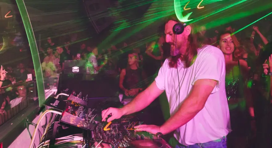DJ w białej koszulce grający na konsoli w klubie z zielonymi laserami.