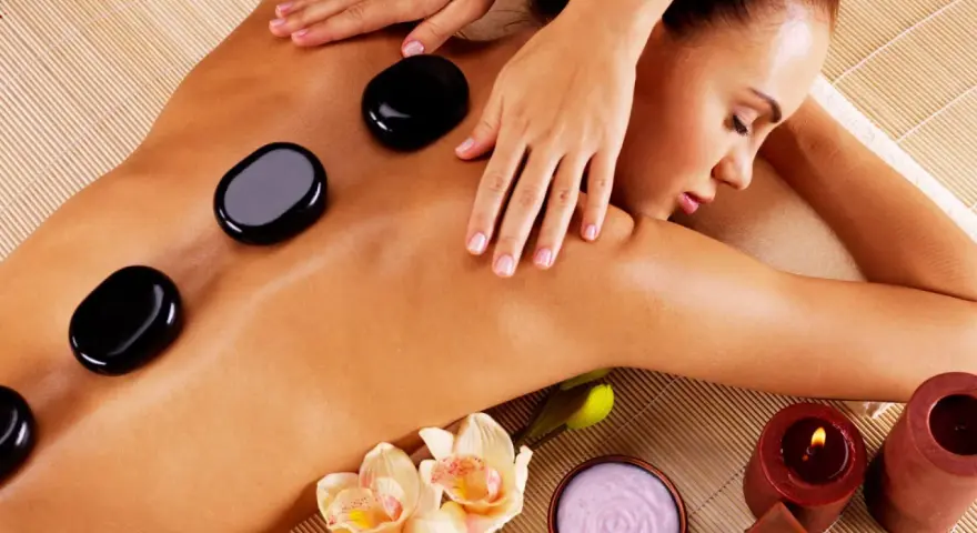 A woman enjoys the benefits of hot stone massage, with smooth black stones placed on her back. Orchids and candles add to the serene spa atmosphere.