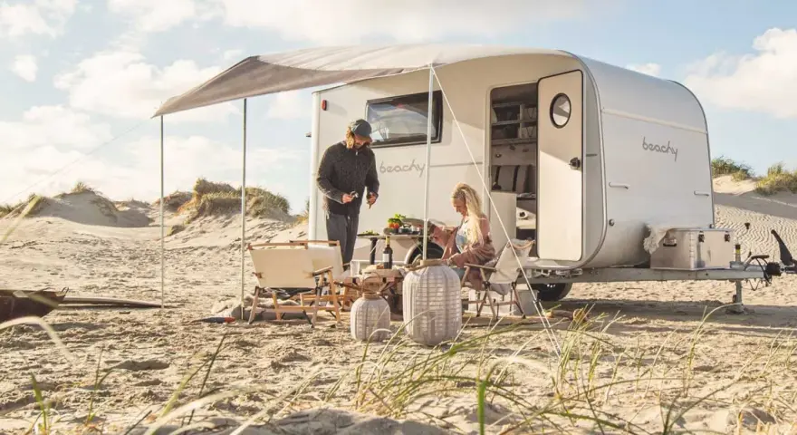 Ett par njuter av en stranddag med sina tyska husvagnar. Solen skiner och sanddynerna skapar en vacker bakgrund.
