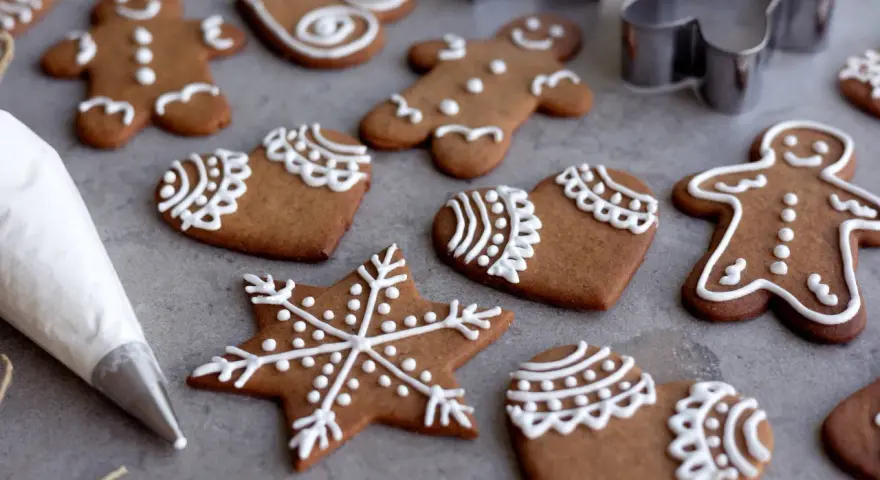Pepparkakshus och hjärtan dekorerade med vit kristyr. En sprits med kristyr ligger bredvid.