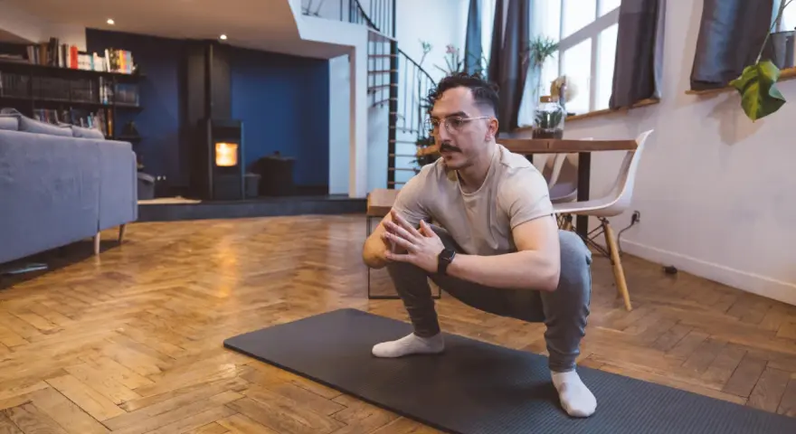 Homme en tenue de sport effectuant un étirement pubalgie sur un tapis de yoga dans un salon moderne.
