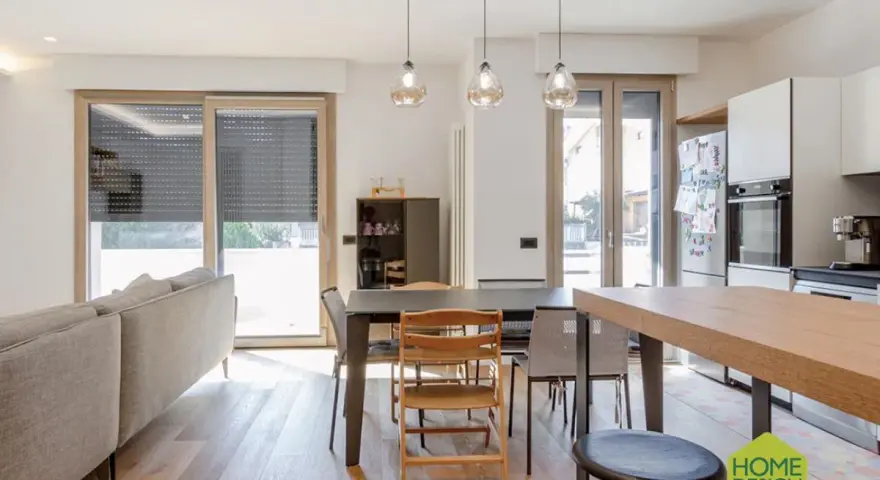 Un soggiorno luminoso con un divano, tavolo da pranzo e cucina a vista. Un moderno sopraluce illumina l'ambiente.