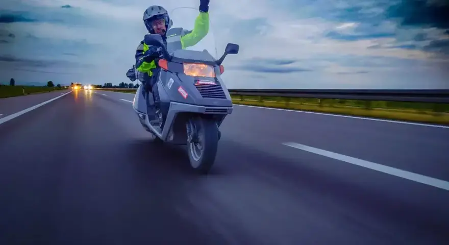Karta motorowerowa w akcji! Kierowca w kasku i kamizelce odblaskowej pozdrawia, jadąc skuterem po autostradzie.