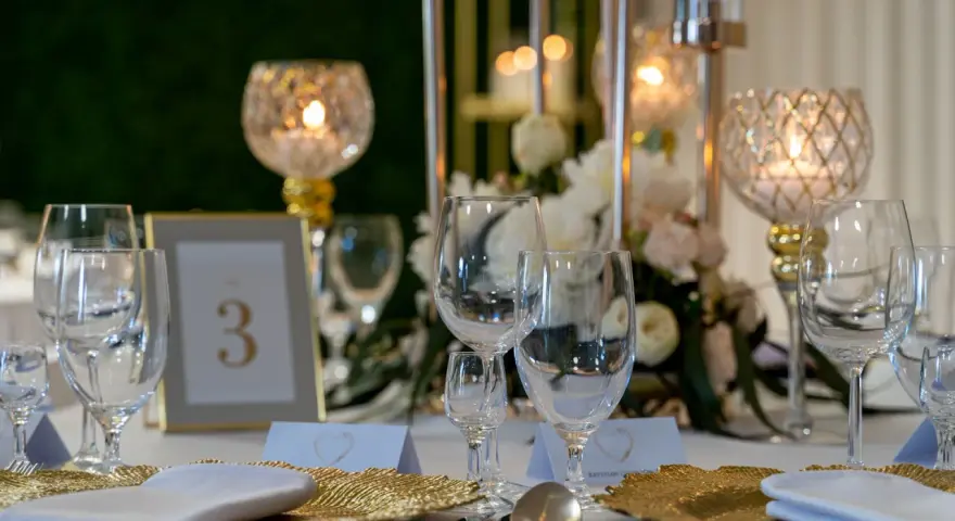 Elegancko nakryty stół weselny z kieliszkami, złotymi talerzami i świecami. Czy warto personalizować każdy element wesela od serwetek po etykiety? Tak!
