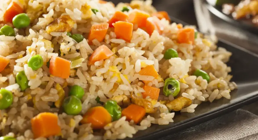 Arroz tres delicias con guisantes y zanahoria en un plato negro.