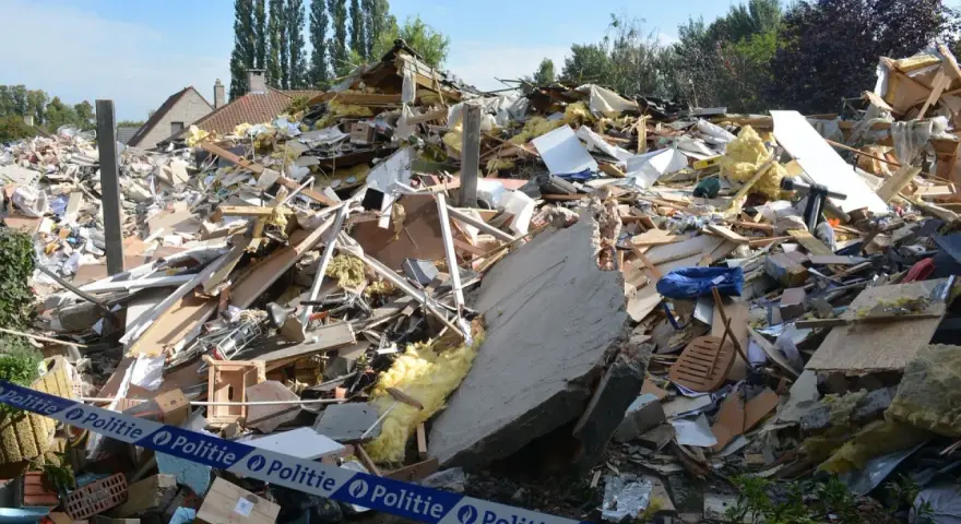 Ogromna kupa gruzów po zawaleniu się budynku. Widać izolację, drewno, beton i niebieską torbę. Wstęga policyjna zabezpiecza teren.
