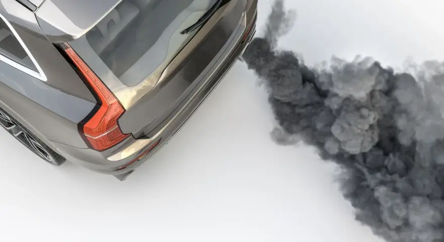 Ein graues Auto stößt beim Gas geben schwarzen Rauch aus dem Auspuff.