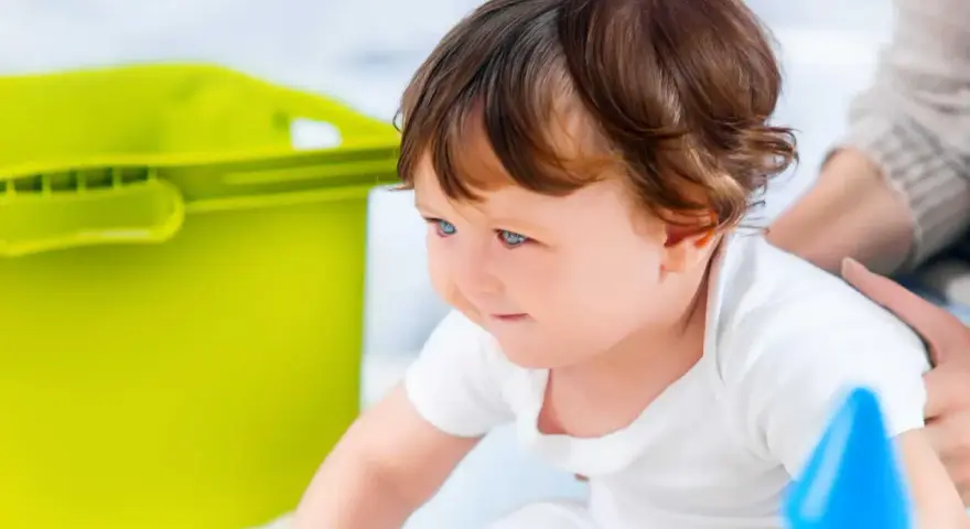Mały poszukiwacz sensoryczny z zaciekawieniem odkrywa świat, obok niego zielony pojemnik i kolorowe zabawki.