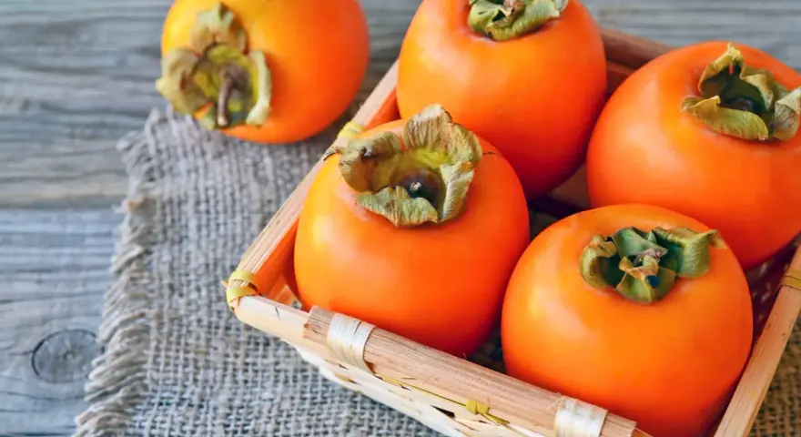 Frische, orangefarbene Kaki-Früchte liegen in einem kleinen Korb auf grobem Leinen. Kaki gesund und lecker.