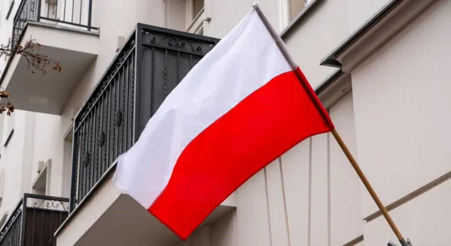 Flaga Polski w pionie, biało-czerwona, powiewa na tle budynku z balkonem.