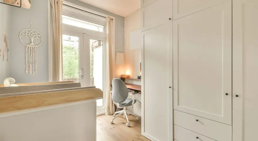 Un angolo studio in camera da letto, con scrivania, sedia girevole e armadio bianco.