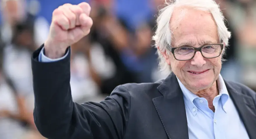 Ken Loach, regista inglese famoso, alza il pugno in segno di vittoria.