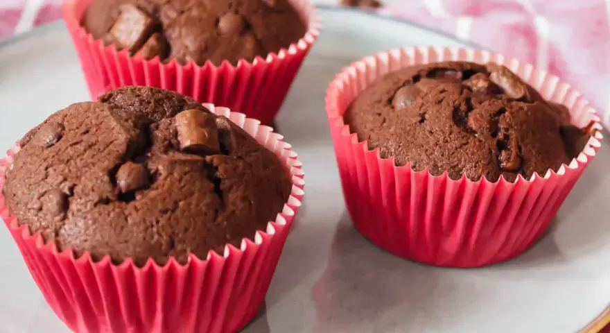 Drei saftige Schokomuffins mit Schokostückchen in roten Papierförmchen, perfekt für Kinder.