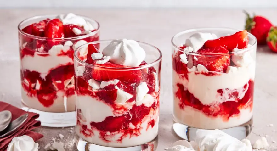 Drei Gläser mit Eton Mess: geschichtete Erdbeeren, Sahne und zerbrochene Baiser-Stücke.