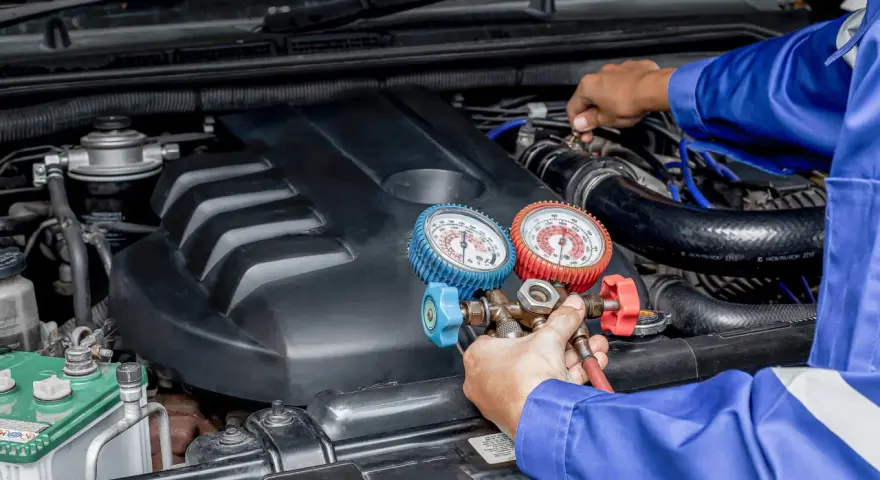 Mecánico realiza carga de gas al aire acondicionado de un coche, usando manómetros para verificar la presión.