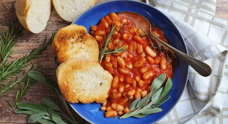 Fagioli all'uccelletto in umido con pomodoro, serviti con pane tostato e erbe aromatiche. Perfetti per scoprire cosa abbinare ai fagioli all'uccelletto.
