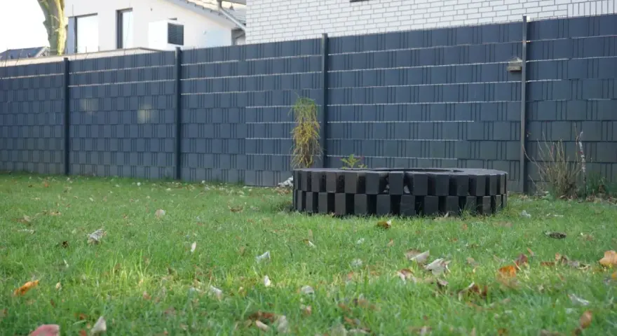 Moderner Sichtschutzzaun, der sich gut zum zaun selber bauen billig eignet. Ein dekorativer Kreis aus schwarzen Steinen im Garten.