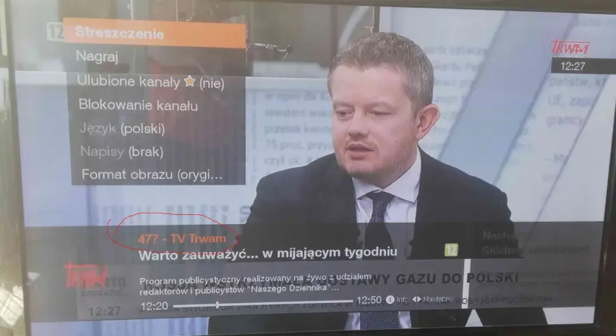 Mężczyzna w garniturze na ekranie telewizora, na którym widać menu z opcją "477 - TV Trwam".
