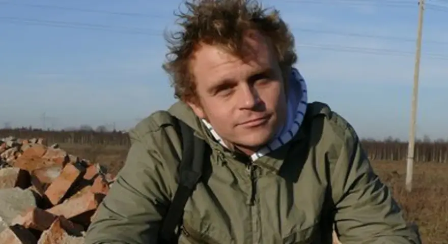 Piotr Rogucki, w otoczeniu gruzu, z charakterystyczną fryzurą, jakby inspirowany swoimi utworami.