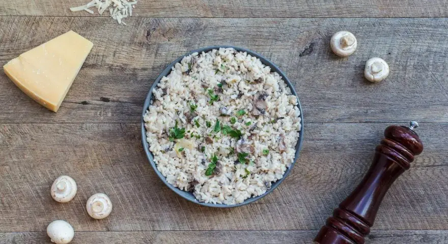 Risotto z grzybami i parmezanem – idealne danie, co można zamrozić na obiad. Obok świeże pieczarki i młynek do pieprzu.