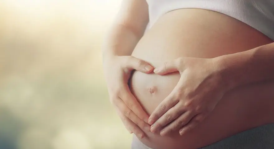 Czekając na dziecko, zastanawiasz się, czy autyzm można wykryć w ciąży? Dłonie tworzą serce na brzuchu.