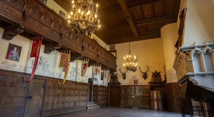 Wnętrze zamku Czocha z bogatymi zdobieniami, portretem króla i banerami. Bilety do zamku czekają na odkrycie jego historii.
