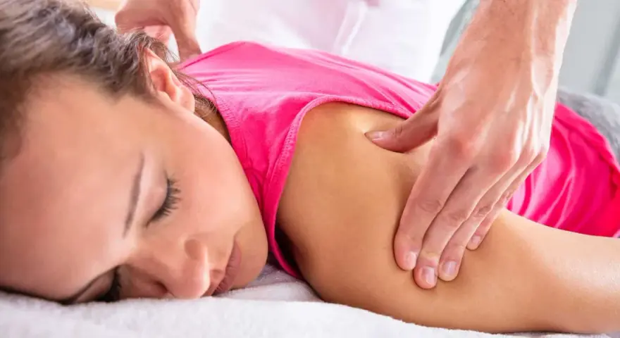 Fizjoterapeuta masuje ramię kobiety, łagodząc ból mięśniowo powięziowy.