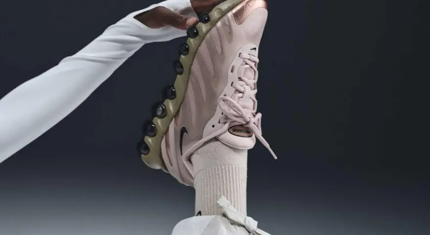 Różowy but Nike na obcasie, trzymany przez dłoń w białej rękawiczce.