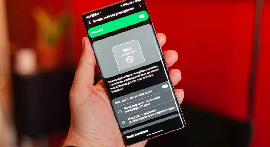 Dłoń trzyma smartfon z włączoną ochroną przed spamem. Ekran pokazuje powiadomienie o potencjalnym spamerze, gdy dzwonią z laboratorium.